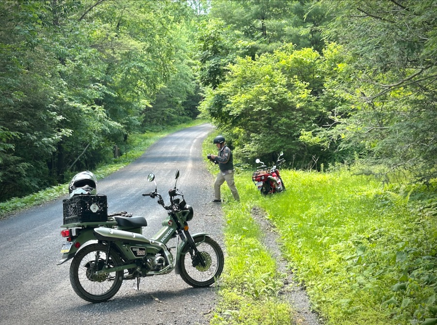 Two Honda Trail 125 motorcycles parked along a gravel road.