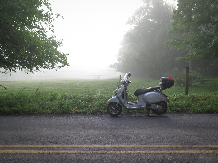 A Vespa GTS 250ie scooter parked next to a foggy field.