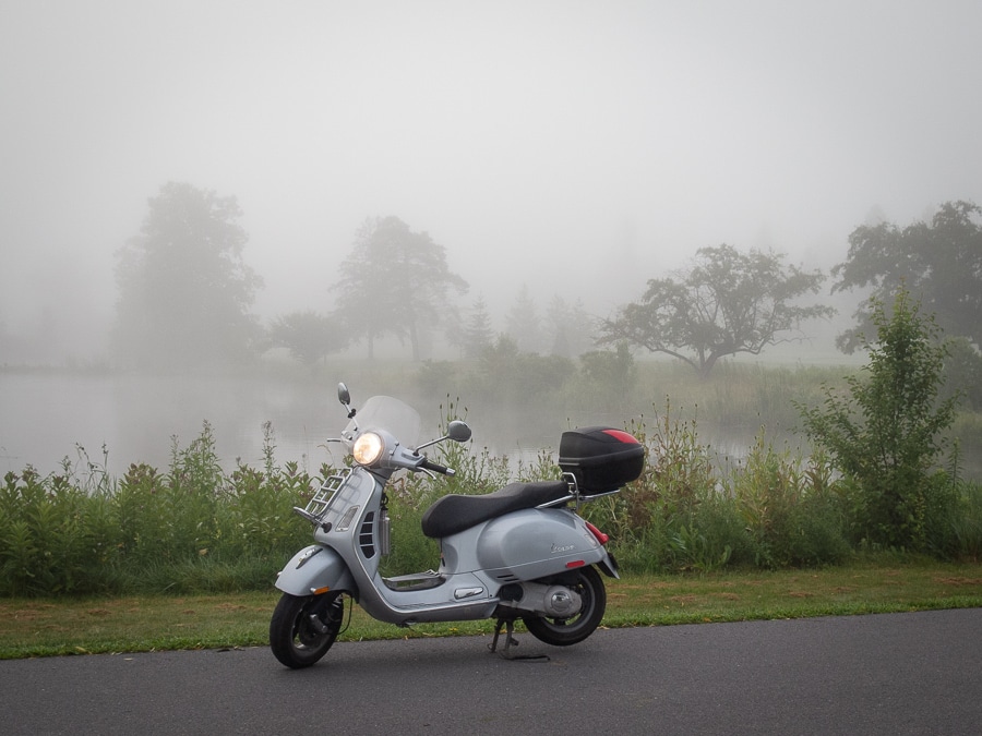 Vespa scooter with fog drifting over a pond.