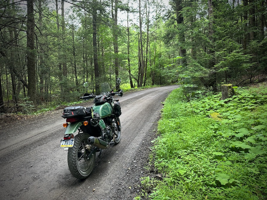 A 2022 Royal Enfield Himalayan on a wet dirt road in a forest.