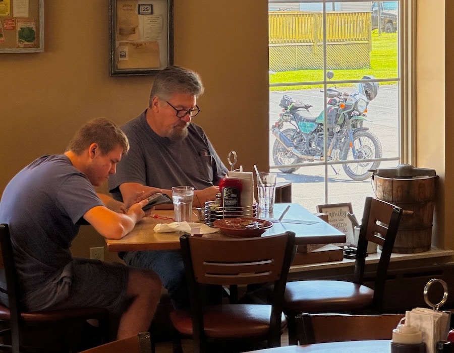 Father and son sitting at a restaurant table looking at their phones.