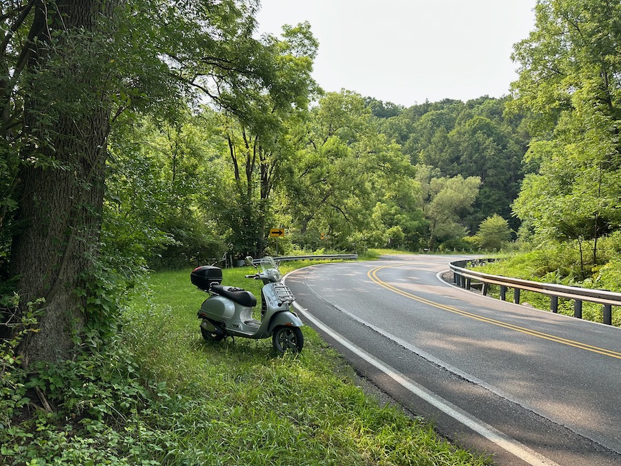 A 2006 Vespa GTS 250 scooter parked along a rural road.