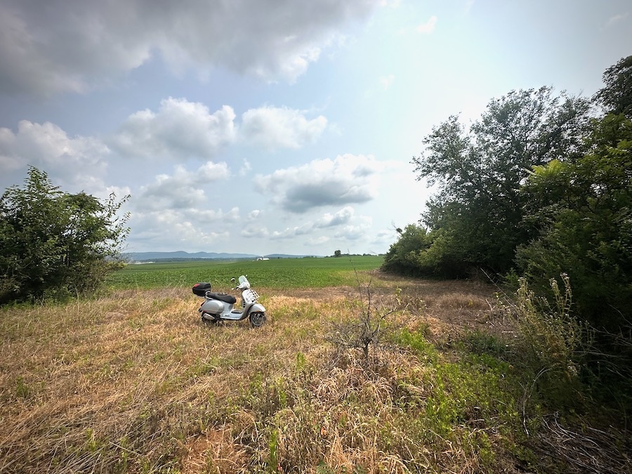 A Vespa scooter parked next to a farm field.