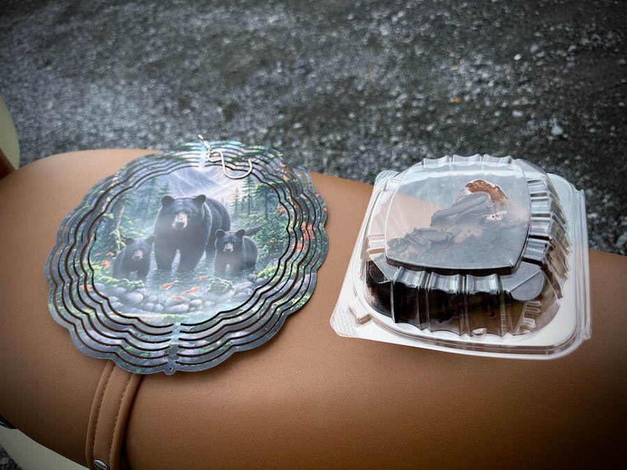 A black bear ornament and piece of chocolate cake on the seat of a Vespa scooter.