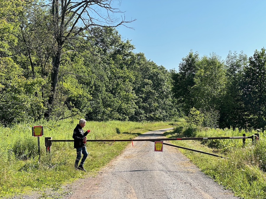 A man standing at a gate on a gravel forest road.