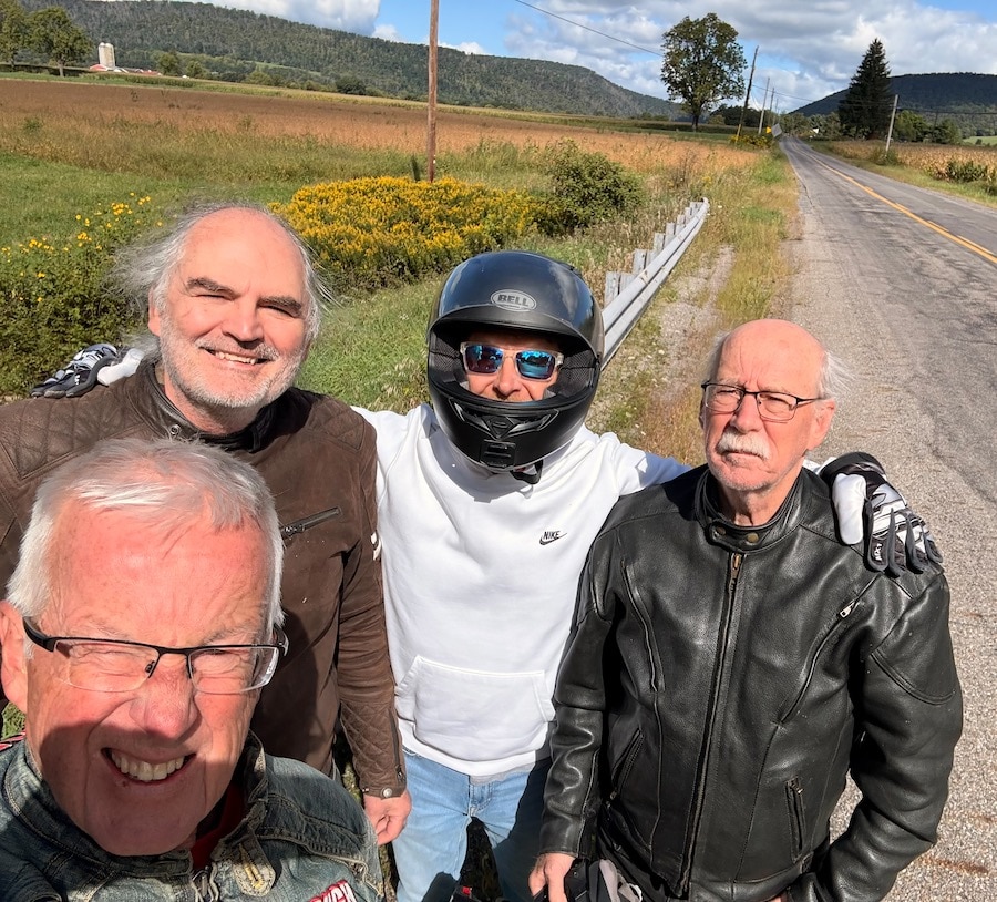 Four motorcycle riders along posing for a group picture.