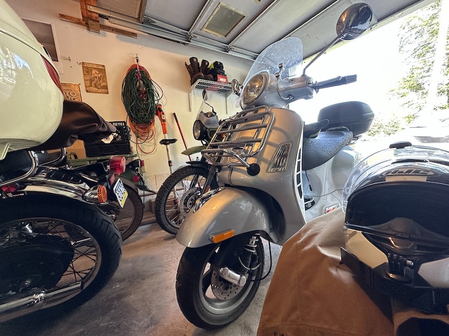 A 2006 Vespa GTS 250ie scooter parked in a garage with other scooters and motorcycles.