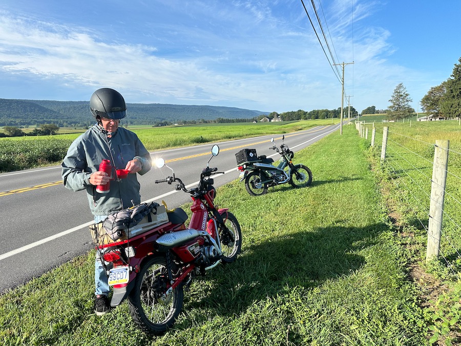 Man pouring coffee from a Thermos while standing next to his motorcycle.