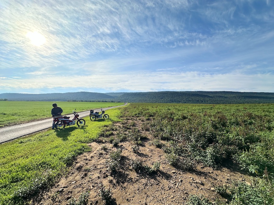 Two small motorcycles parked along a narrow rural road.