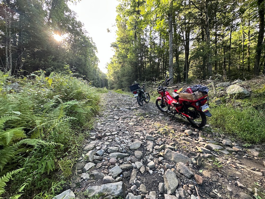 Two Honda Trail 125 motorcycles parked along a rough mountain trail.