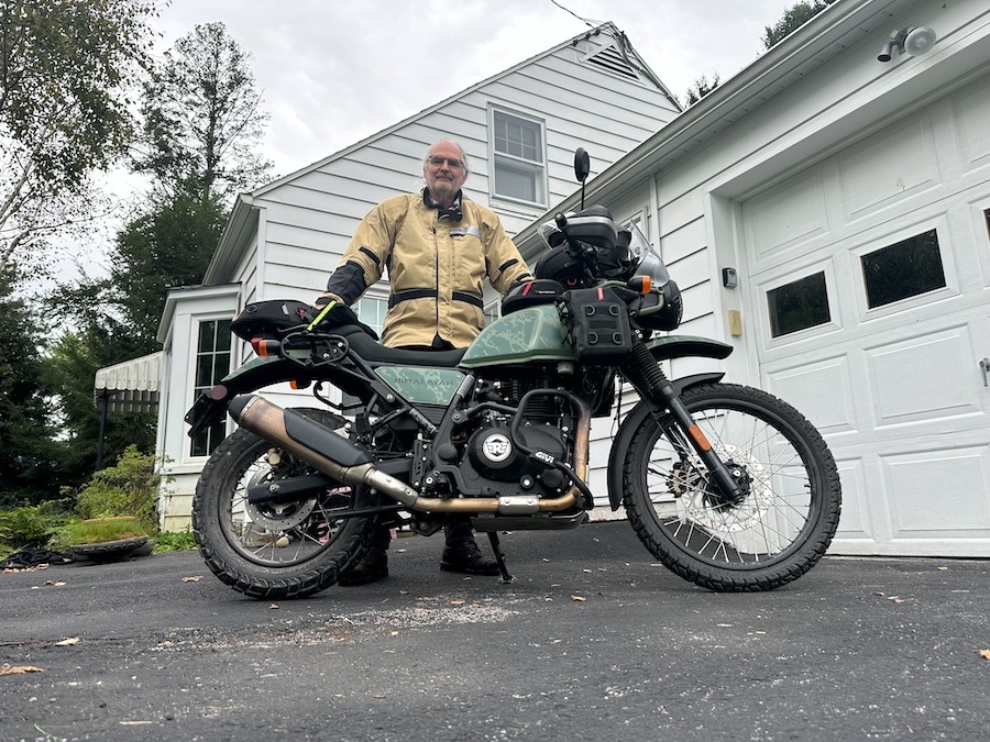 Man wearing an Aerostich Darien jacket standing with a Royal Enfield Himalayan motorcycle.
