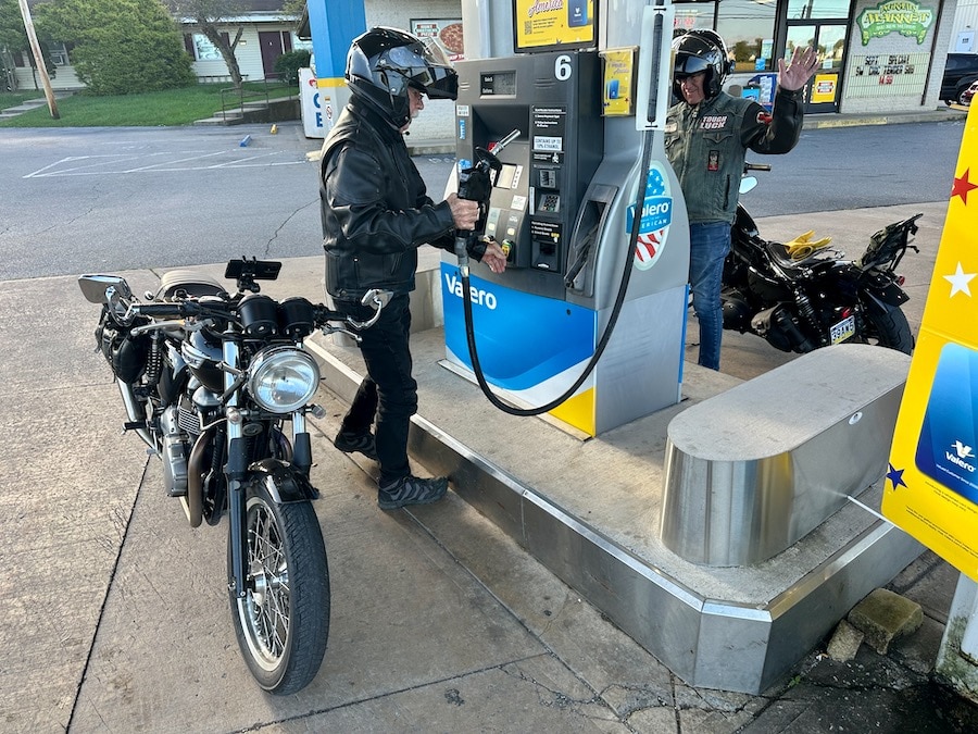 Two men getting gas for their motorcycles.