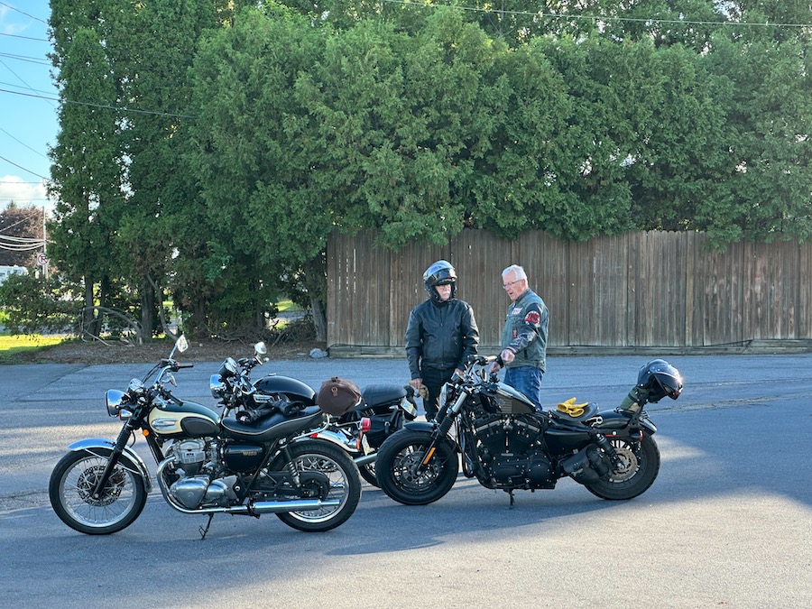 Two men discussing motorcycles in a parking lot.
