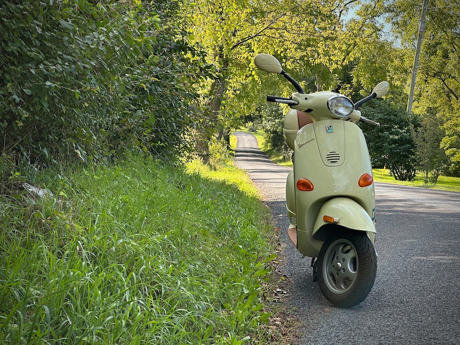 A Vespa ET4 parked along a tree lined road.