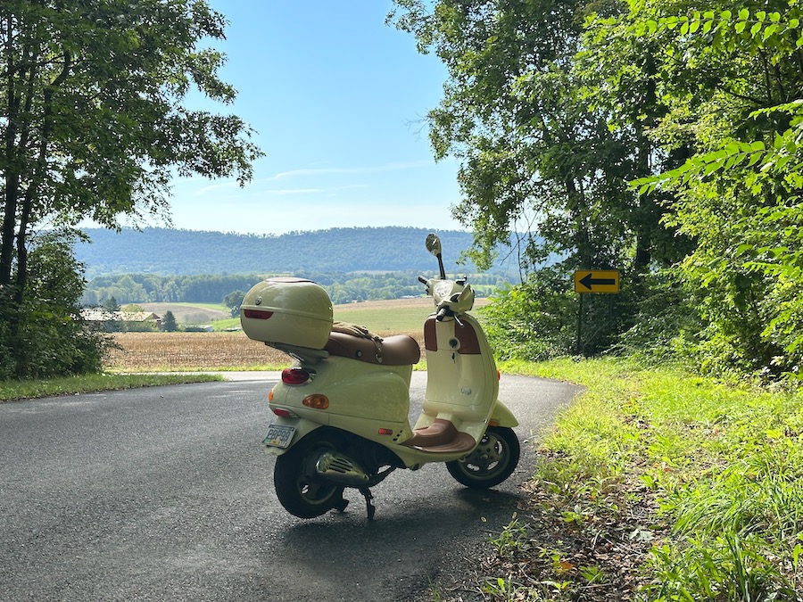 A Vespa ET4 parked along a rural road on a beautiful morning.