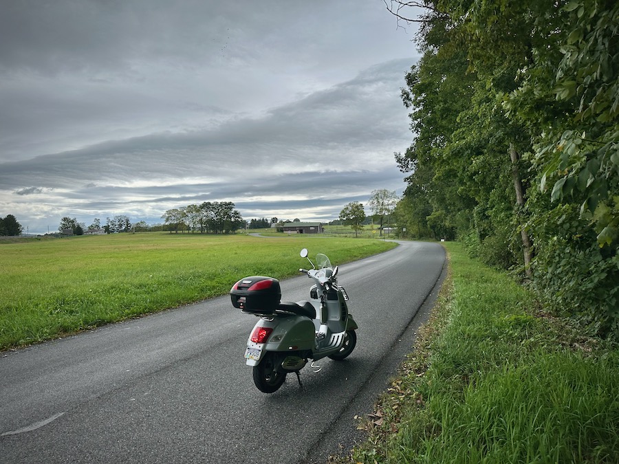 A 2006 Vespa GTS 250 scooter on a rural road on an overcast day.