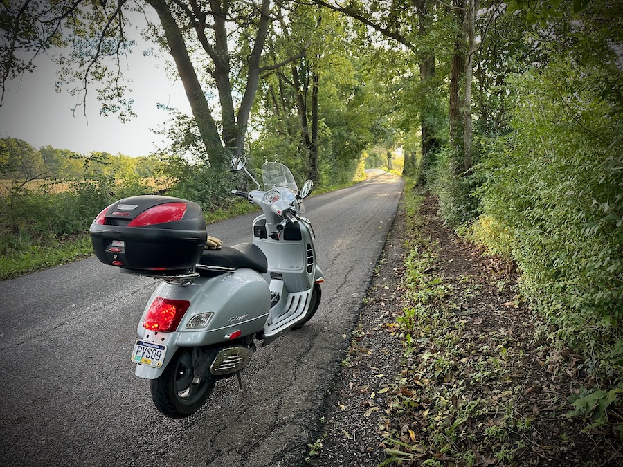 A Vespa GTS scooter parked on a rural road in the morning.