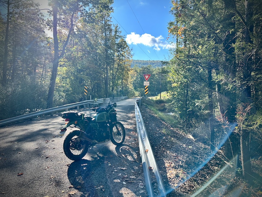 A Royal Enfield Himalayan motorcycle parked near a small bridge in brilliant morning sunlight.