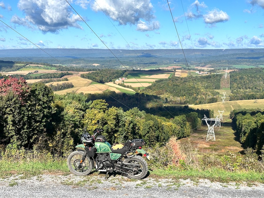 A Royal Enfield Himalayan motorcycle parked at a power line cut to admire the view.