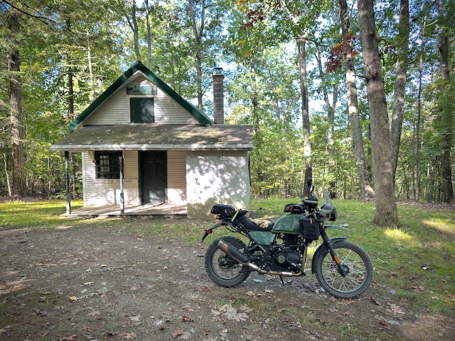 A Royal Enfield Himalayan motorcycle parked in front of a small cabin in Rothrock State Forest.