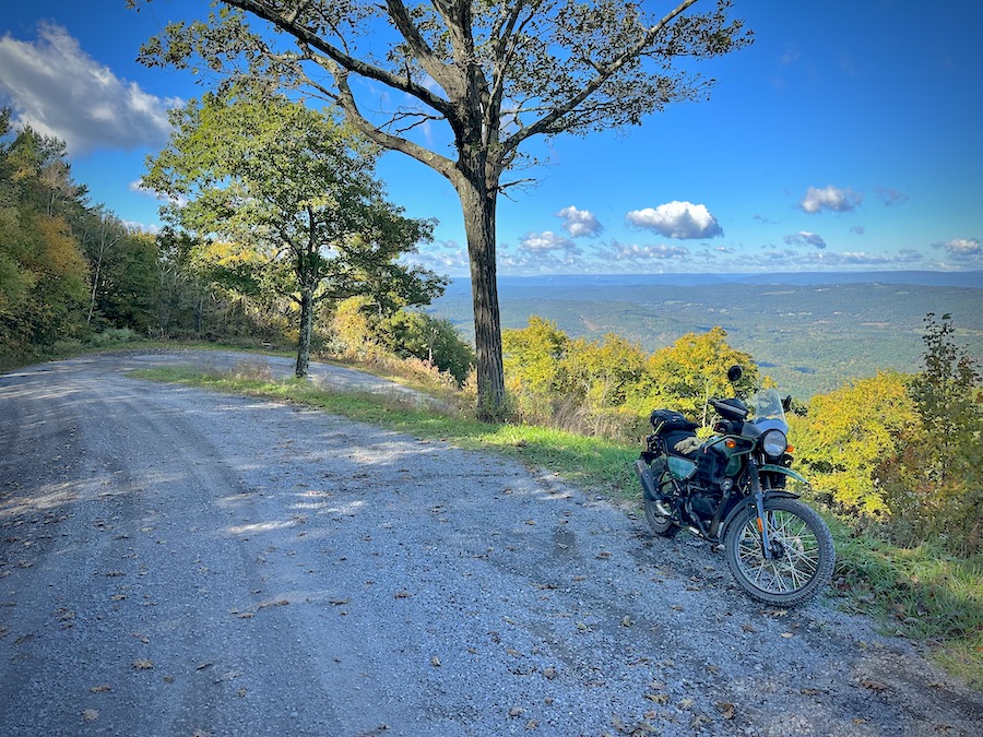 A motorcycle parked along a mountain road with a sweeping vista.