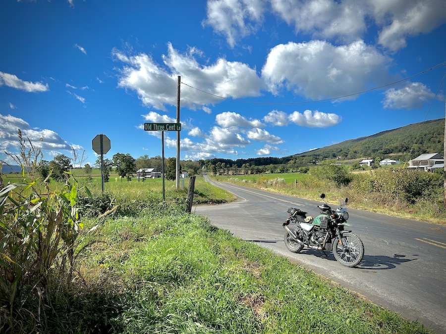 A Royal Enfield Himalayan motorcycle parked at a rural intersection in an agricultural valley.