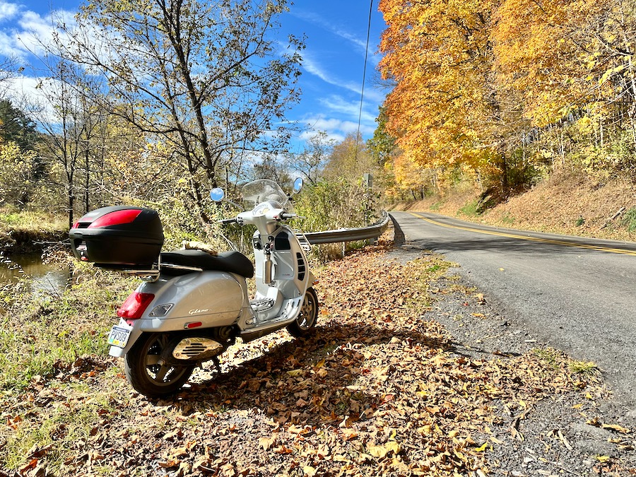 A 2006 Vespa GTS 250 scooter parked along a rural road in autumn.